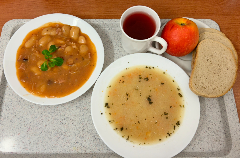 Na zdjęciu znajduje się: Barszcz biały z ziemniakami, Chleb mieszany pszenno-żytni, Fasolka po bretońsku, Jabłko, Kompot owocowy